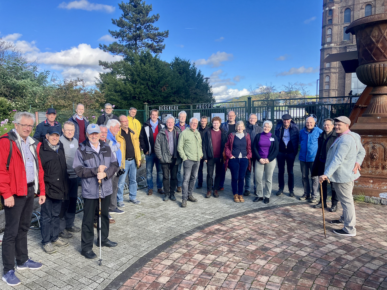 Eine große Gruppe an Personen steht vor einem Gebäude, im Hintergrund der Schriftzug "Bergwerk"