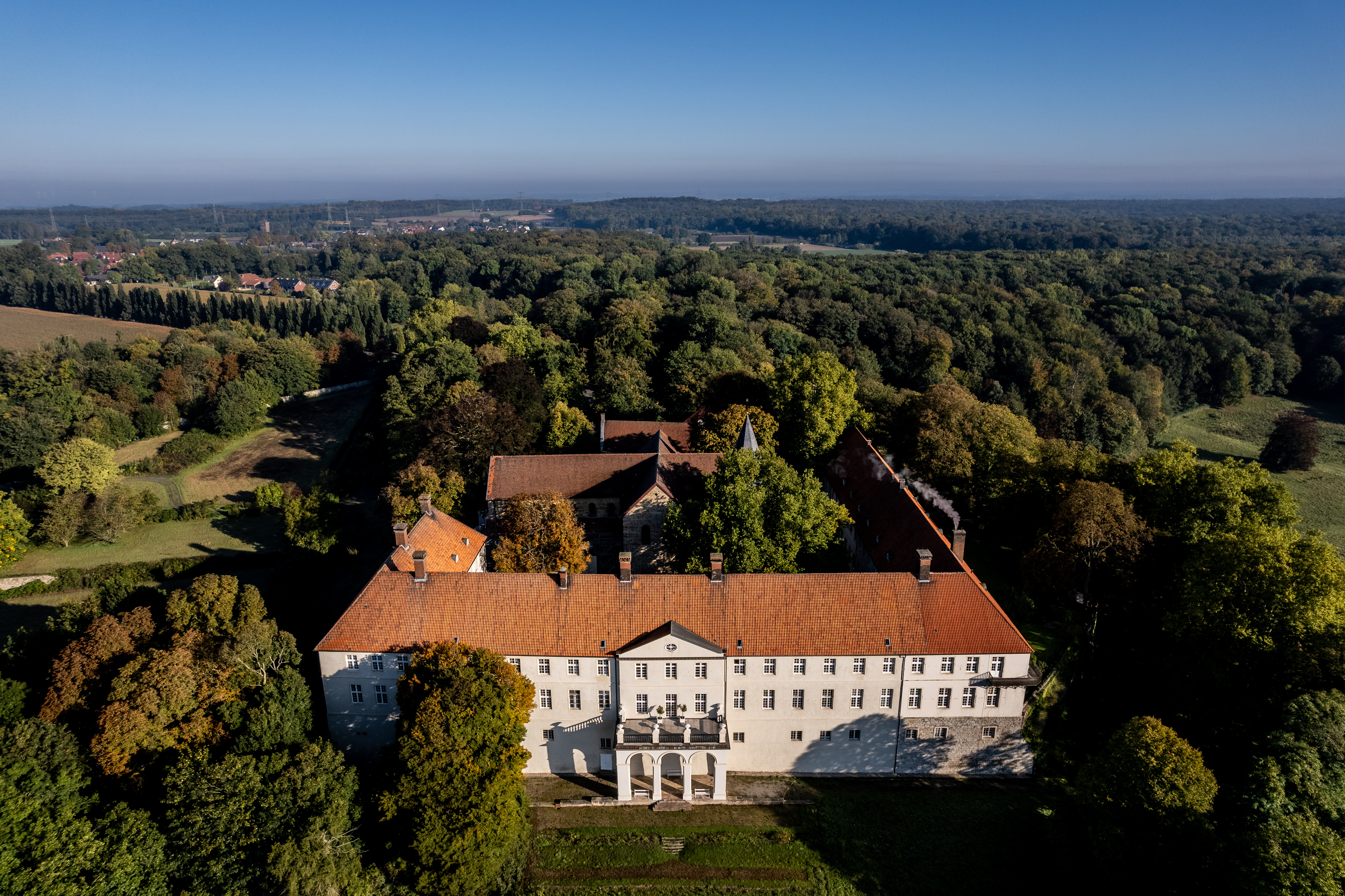 Schlossgebäude von oben, umgeben von grünen Wäldern