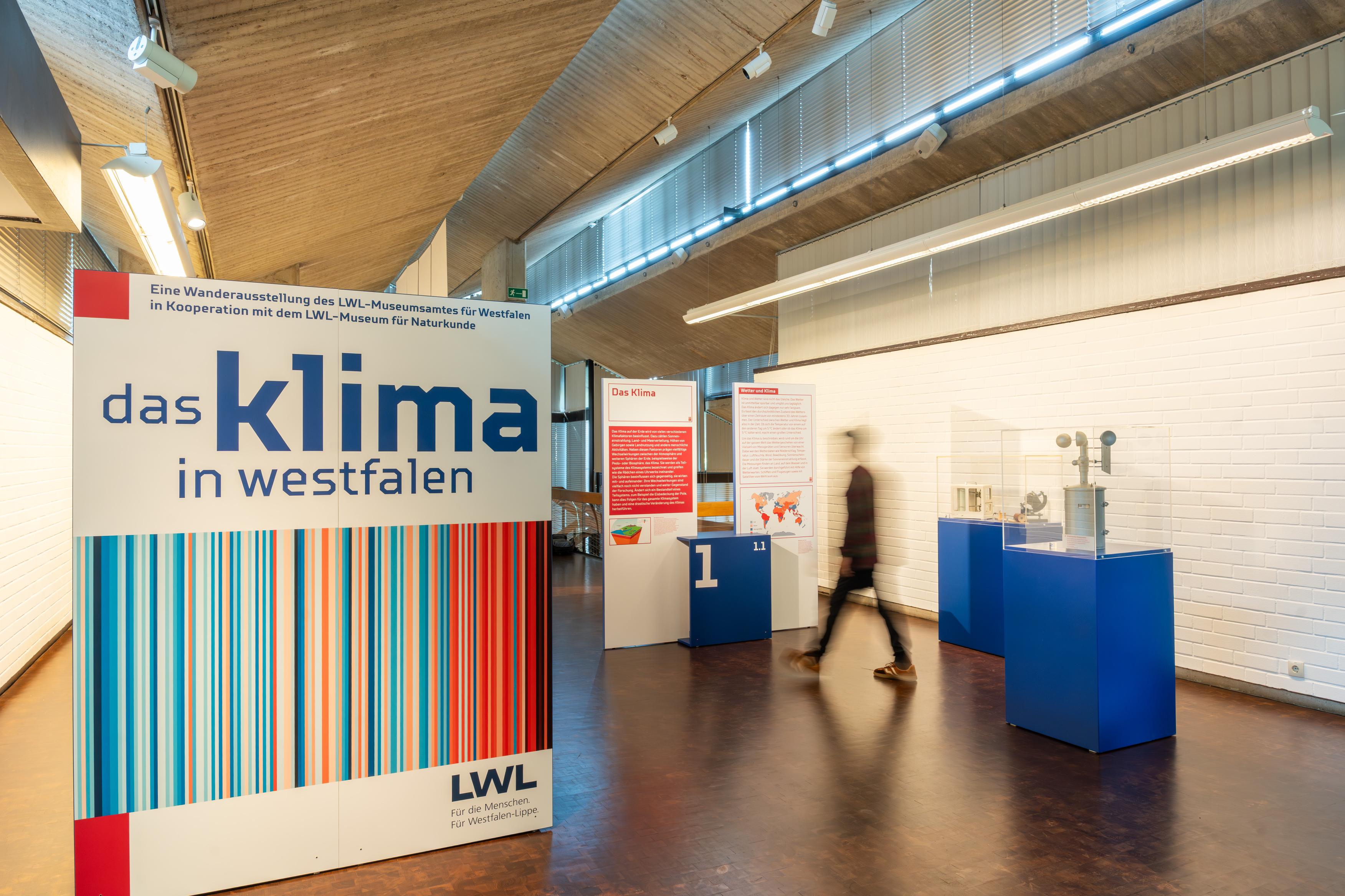 Ausstellungsraum mit großem Schild zur Wanderausstellung "das klima in westfalen" und mehreren blauen Vitrinen mit Exponaten
