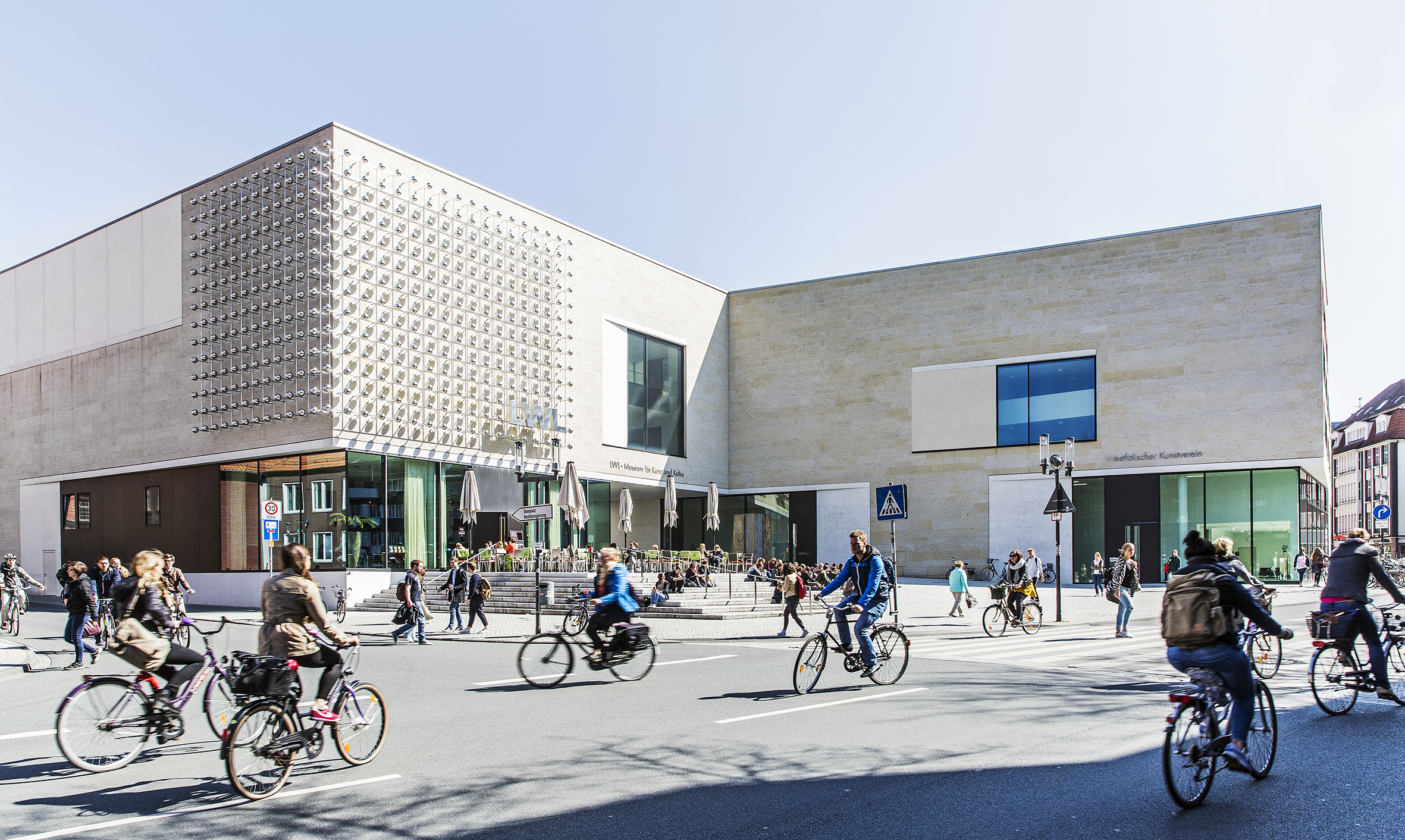 Die Südfassade des LWL-Museums für Kunst und Kultur in Münster mit Blick auf die Straße, auf der viele Fahrradfahrer:innen unterwegs sind.