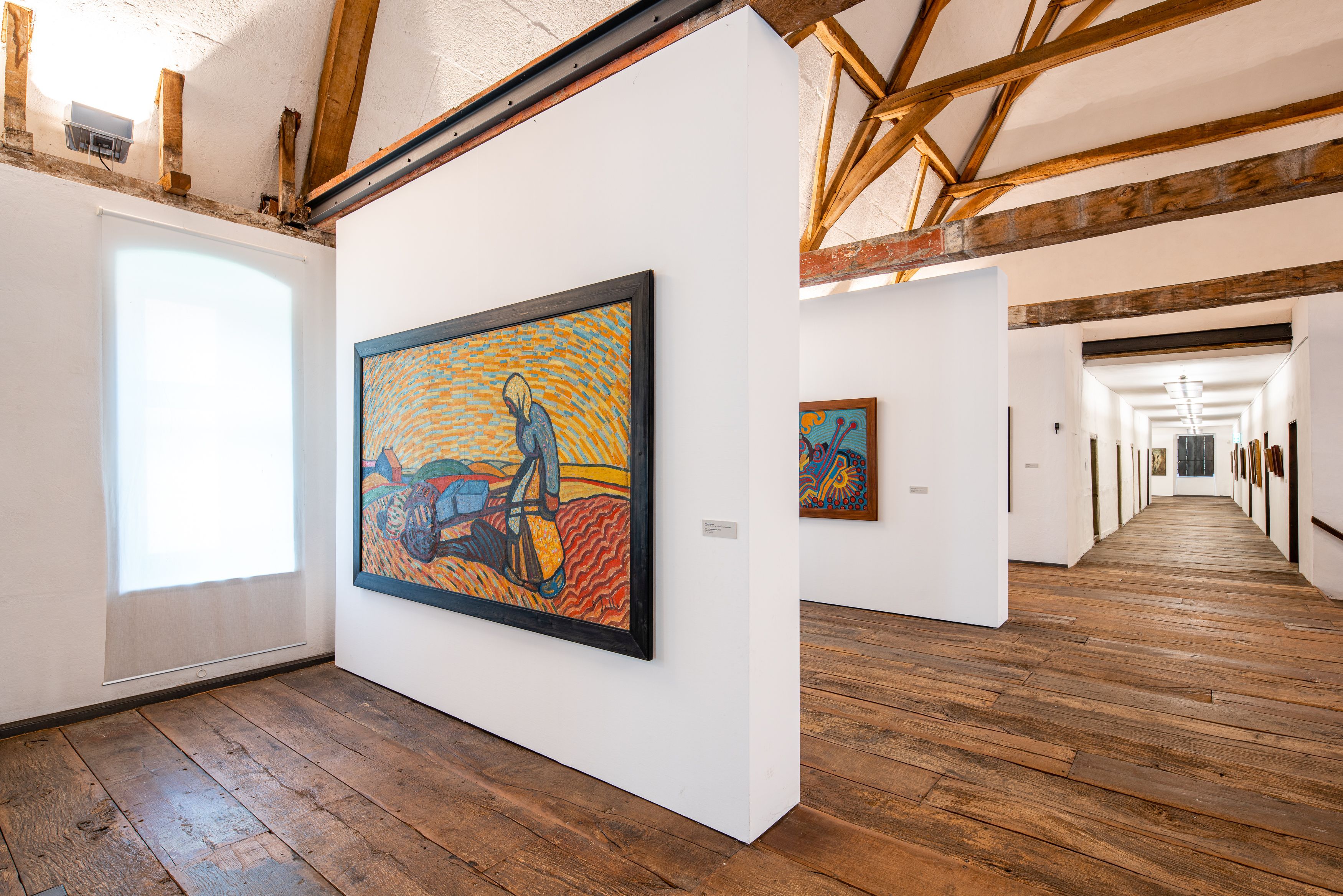Galerieraum mit Gemälden an der Wand und hölzernen Dachbalken