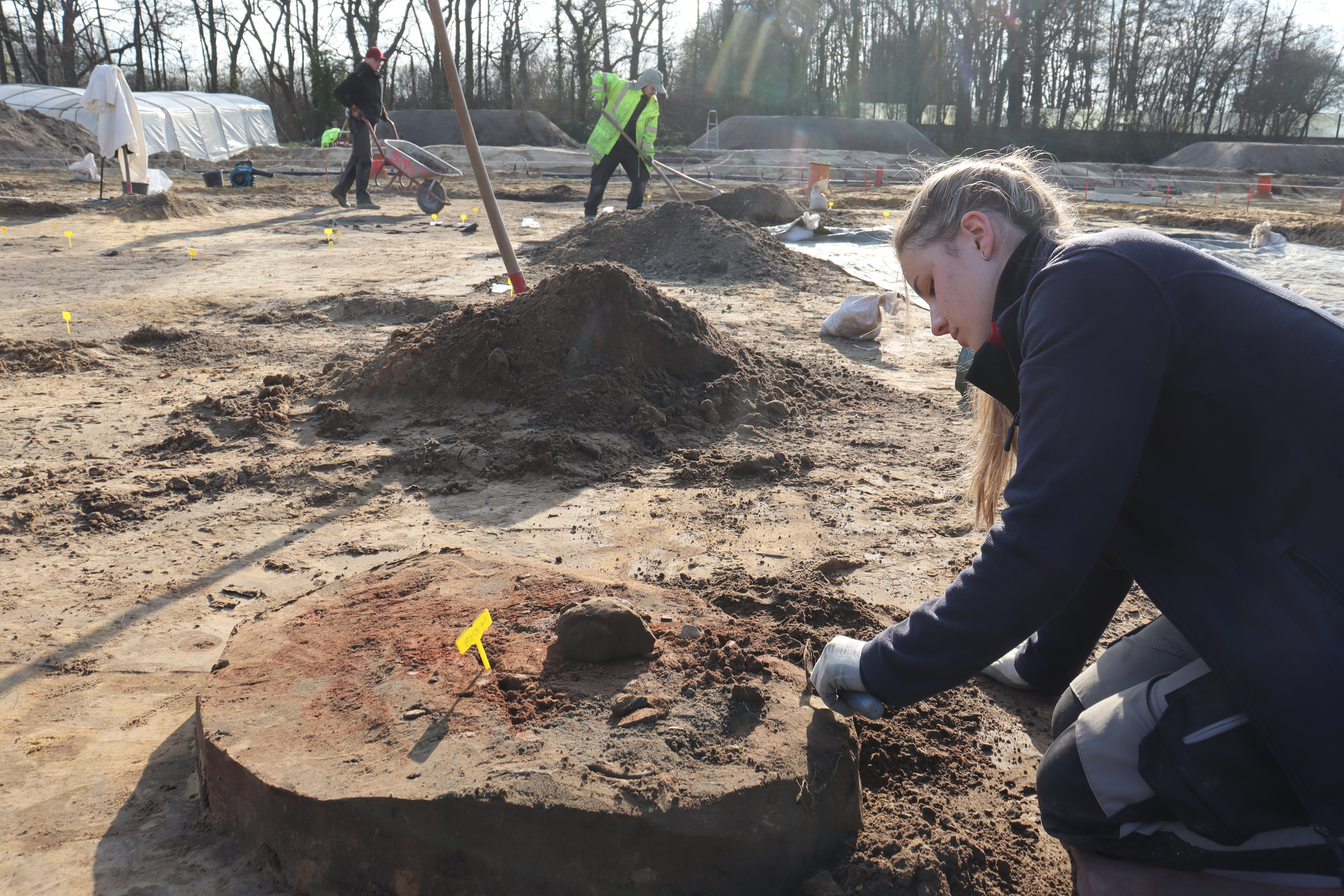 Eine Frau auf einem archäologischen Ausgrabungsfeld legt Funde frei.