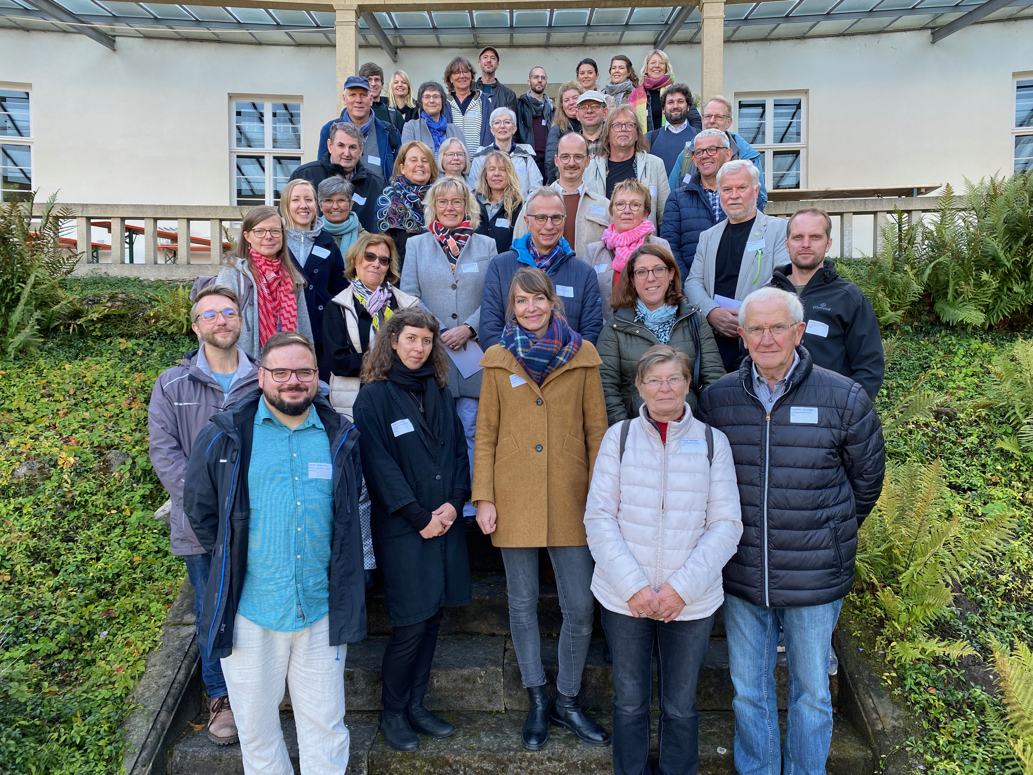Gruppenfoto von mehreren Personen auf einer Außentreppe vor einem Gebäude mit Fenstern und Geländer