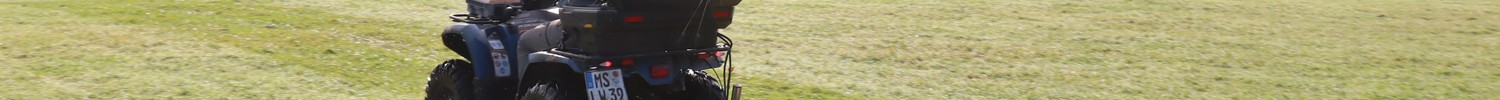Person auf einem Quad mit angehängtem Bodenradargerät auf einer Wiese vor bewaldeten Hügeln