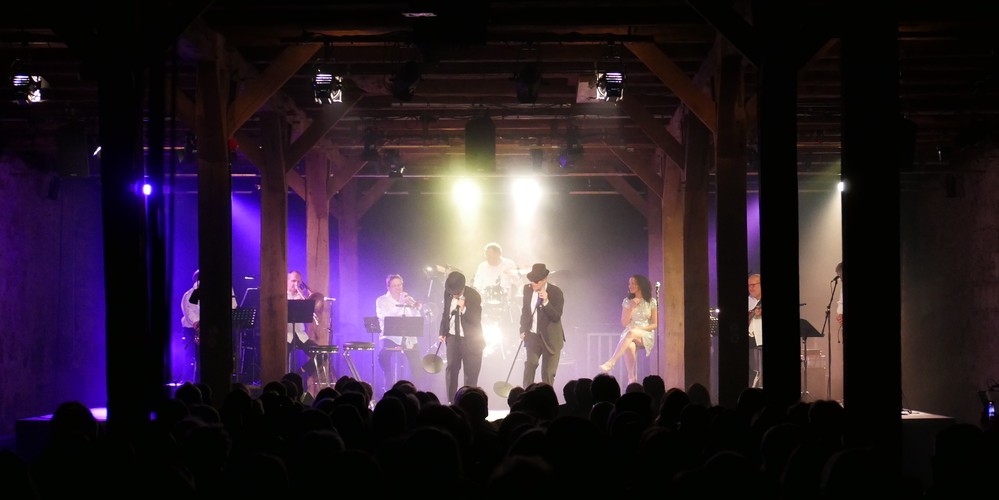 Eine beleuchtete Bühne mit Musikern in einem dunklen Raum mit Publikum