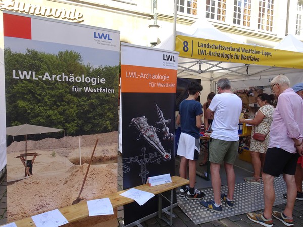 Menschen an einem Informationsstand mit Bannern mit der Aufschrift "LWL-Archäologie für Westfalen"