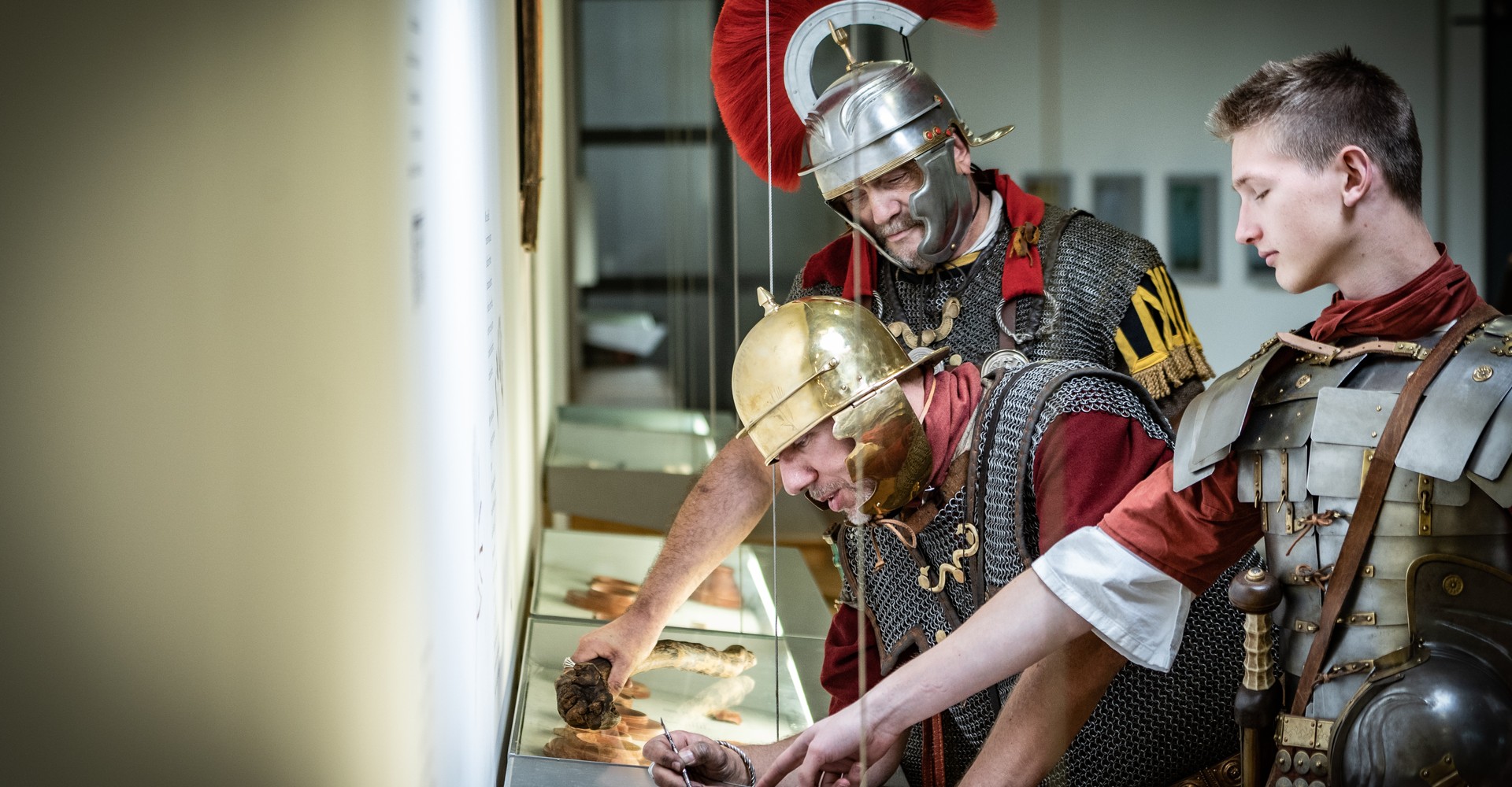 Drei Menschen, verkleidet als römische Legionäre, probieren Wachstafeln in der Dauerausstellung aus.