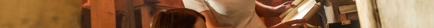 Zwei Personen lösen gemeinsam ein Rätsel in einem Escape-Room mit antik wirkender Kulisse und Holzdecke.