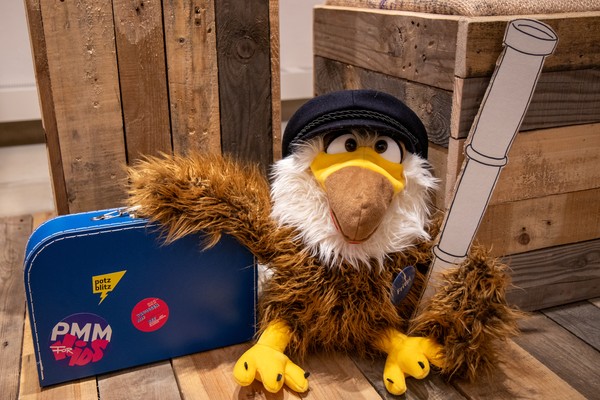 Ein Kuscheltieradler mit einer Seemannsmütze, einem Koffer und einem Fernrohr.