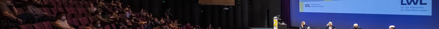 Bühnenraum des Stadttheaters Münsters mit Publikum gefüllte Sitzreihen, Blick auf die Bühne mit stattfindender Podiumsdiskussion