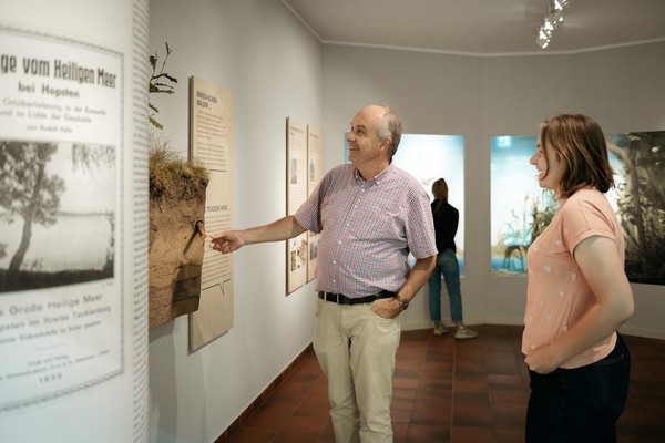 Zwei Personen stehen in einem Ausstellungsraum vor einer Informationstafel