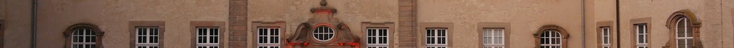 Große Menschenmenge sitzt vor einem historischen Gebäude mit vielen Fenstern und einem Uhrturm auf dem Dach