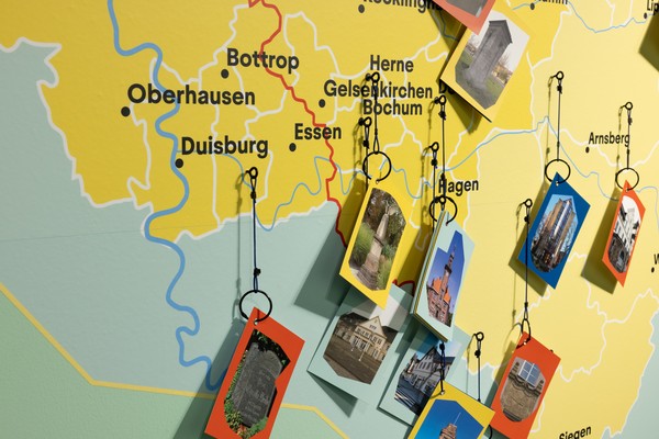 Landkarte des Ruhrgebiets mit Städtenamen und an Schnüren hängenden Fotos von Gebäuden und Objekten