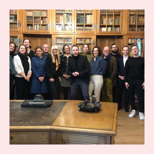 Gruppenfoto von etwa 15 Personen in einem historischen Raum mit hohen Holzregalen voller Bücher, vor einem großen Holztisch, alle in die Kamera blickend.