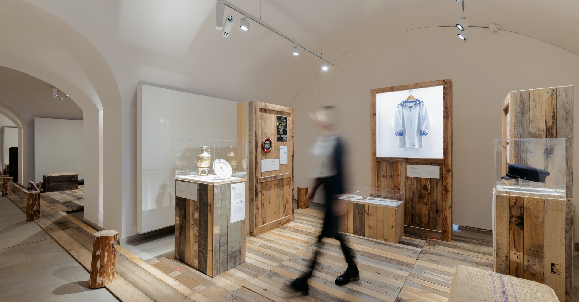 Blick in einen Ausstellungsraum mit Vitrinen und Boden aus Holzplanken