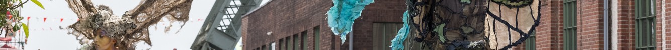 Draußen vor dem Förderturm laufen Menschen und verkleidete Künstler:innen auf Stelzen.