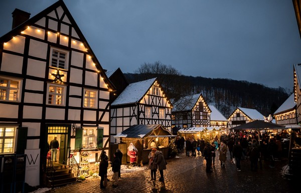 Beleuchteter historischer Weihnachtsmarkt mit Fachwerkhäusern und Menschen bei Dämmerung