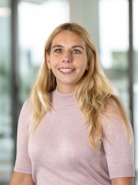 Frau mit langen blonden Haaren und rosa Pullover lächelt vor unscharfem Hintergrund