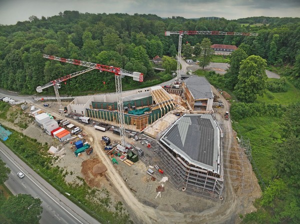 Luftaufnahme einer Baustelle mit mehreren Kränen und Gebäudestrukturen in einem bewaldeten Gebiet
