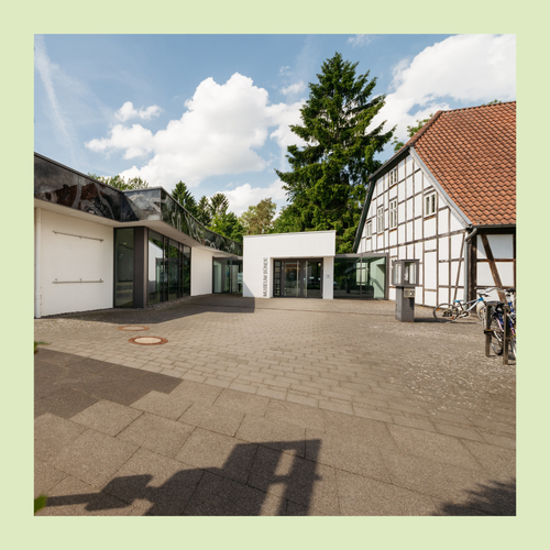 Foto eingefasst in grünem Rahmen. Foto zeigt Blick auf den Museumseingang, links der Neubau und rechts Fachwerkgebäude.