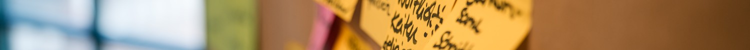 Braunes Papier mit handschriftlichen Notizen und mehreren gelben und rosa Haftnotizen an einer Wand