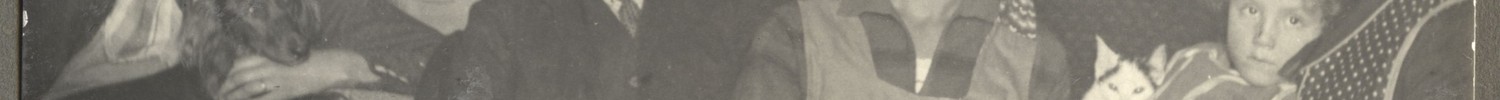 Fünf Personen unterschiedlichen Alters sitzen an einem mit kariertem Tischtuch bedeckten Tisch mit Fotoalben darauf.