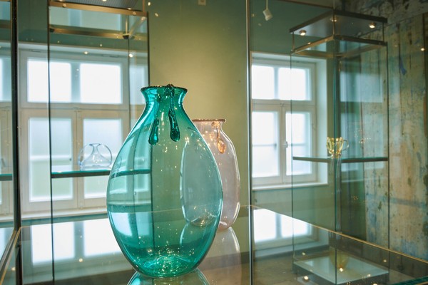 Transparente Glasvasen in verschiedenen Farben auf einem Glasregal vor Fenstern