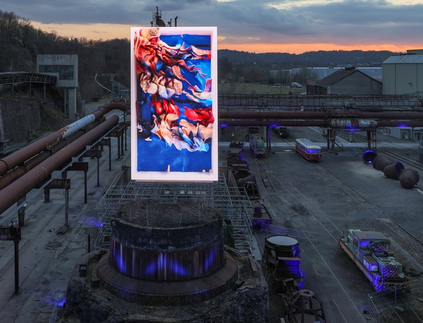 Monumentale digitale Datenskulptur von Refik Anadol mit rot-orangem-blau, fließendem Muster im Industrieareal der Henrichshütte bei Dämmerung.