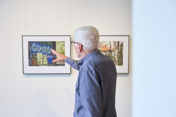 Person in Ausstellungsraum zeigt auf eine Fotografie, die an der Wand hängt