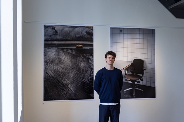 Eine junge Person steht vor zwei großen Fotografien, die an der Wand hängen.