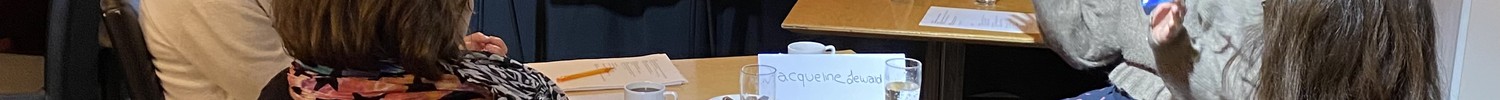 Vier Personen sitzen im Stuhlkreis vor Flipchart mit Überschrift 'PERSONAL' und diskutieren in einem Raum mit Holzboden und schwarzem Hintergrund