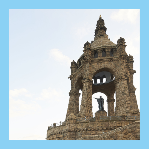 Steinerner Aussichtsturm mit offener Arkadenstruktur und einer stehenden Statue im Inneren, Foto eingefasst von einem blauen Rahmen.