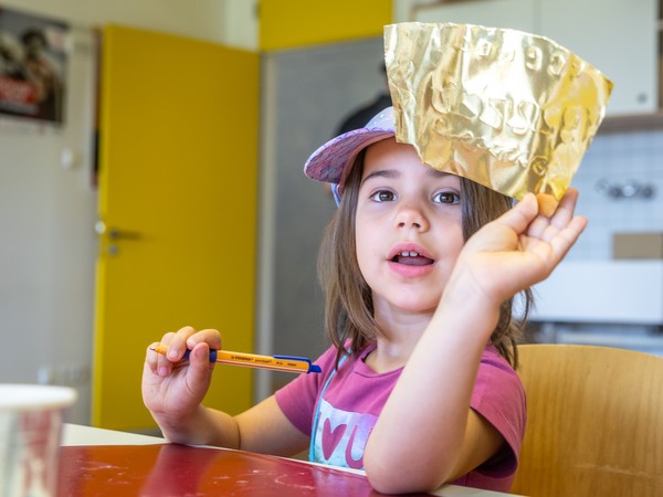 Kind zeigt ein goldenes Papierstück in die Kamera.