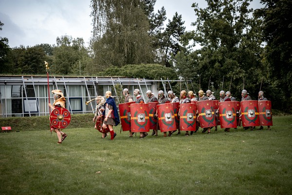 Menschen in Legionärsuniform mit großen Schildern marschieren in zwei Reihen vor dem Museumsgebäude.