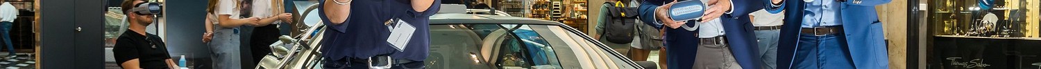 Drei Personen stehen vor einem silbernenAuto in einem Einkaufszentrum und halten VR-Brillen in den Händen.