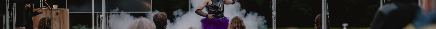 Drag-Künstler:in performt draußen vor Menschen, die auf Gartenstühlen sitzen
