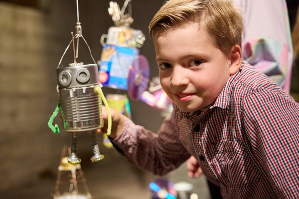 Kind hält selbstgebastelte Roboterfigur aus Dosen und Draht in der Hand.