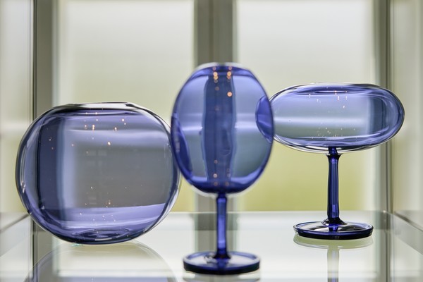 Drei blaue Glasobjekte mit unterschiedlichen Formen auf einer Glasfläche vor einem Fenster