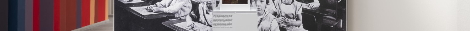 Blick in einen Ausstellungsraum mit einer großen Schwarz-Weiß-Fotografie von Kindern in einem Klassenraum.