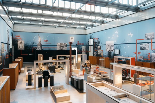 Ein Ausstellungsraum mit Vitrinen und Ausstellungsstücken in der Mitte und einem Zeitstrahl an der Wand.