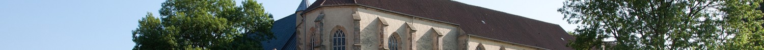 Altes Kirchengebäude und Fachwerkhaus auf einem Hügel mit grüner Wiese
