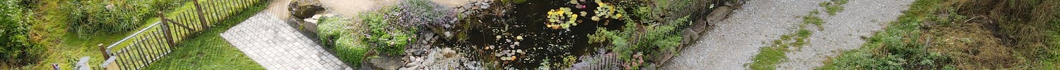 Luftaufnahme eines naturnah gestalteten Gartens mit Teich, Beeten, Wegen und kleinem Bachlauf, umgeben von Wiesen und Bäumen.