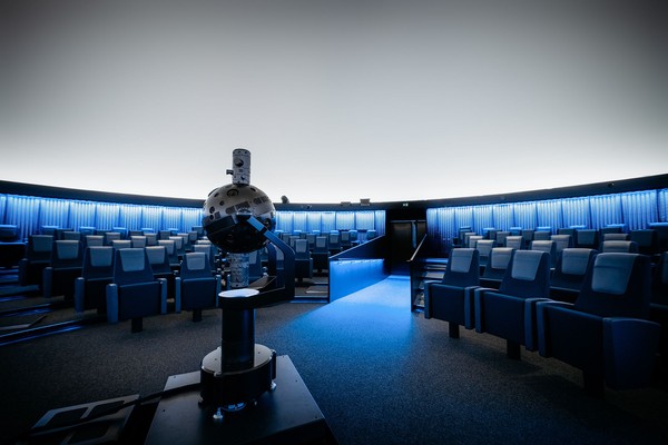 Planetariumsraum mit Sitzreihen und einem zentralen Projektionsgerät unter einer Kuppel