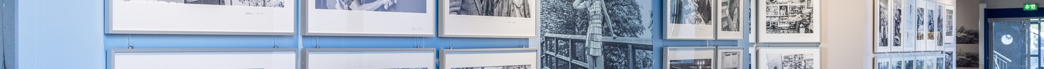 Ausstellung mit schwarz-weißen Fotografien an hellblauen Wänden in einem Raum mit Holzbalken an der Decke