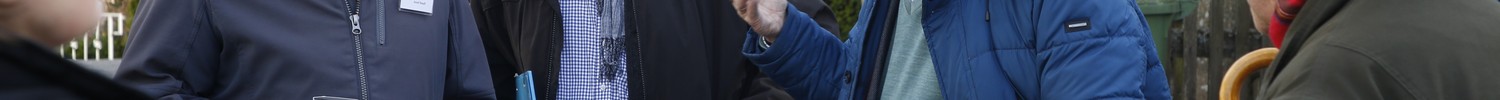 Gruppe von älteren Menschen in Winterkleidung steht im Freien vor Fachwerkhäusern und unterhält sich.
