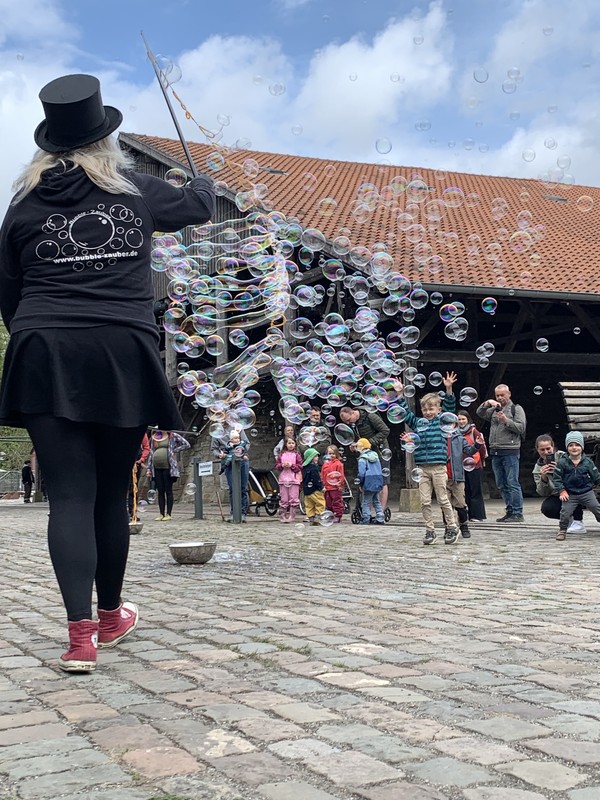 Eine Person macht viele Seifenblasen, ein Kind spielt mit den Seifenblasen