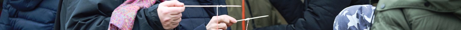 Gruppe von Menschen in Winterkleidung, die zusammenstehen und Stäbe mit Fäden halten
