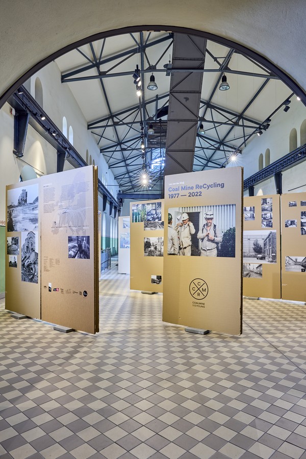 Ausstellung mit großen Informationstafeln zu Bergbau und Recycling in einer Halle mit hohen Fenstern und sichtbaren Stahlträgern im Dachbereich.